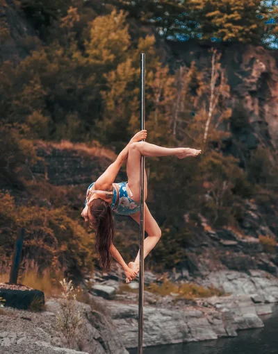 Trainerin zeigt die Figur Brass Monkey Variation an einer Polestange in der Natur.
